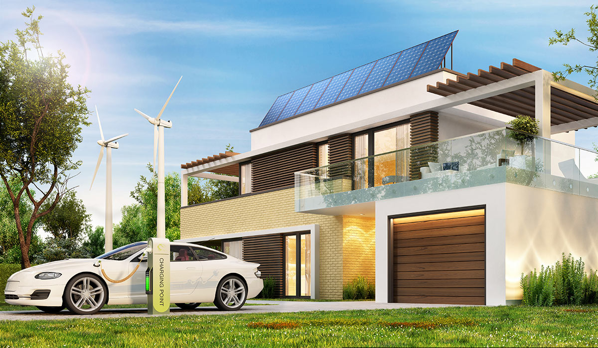 A stock image of an ecological home with wind turbines, solar panels on the roof, and an electric car being charged in front of the house at a charging station.