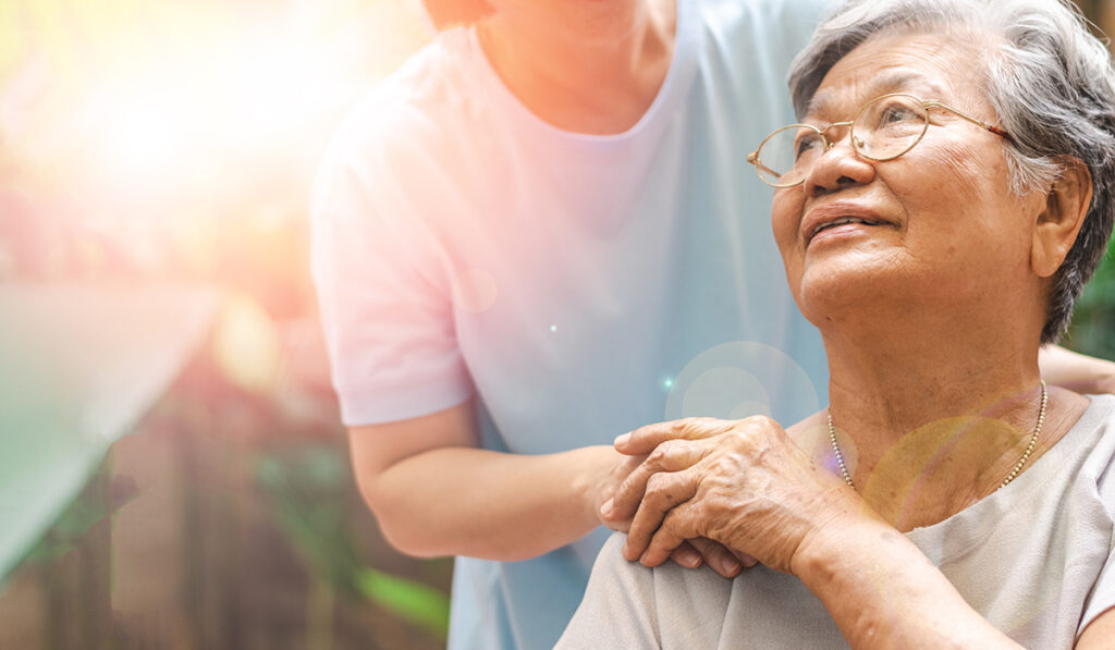An elder patient puts her hand on the hand of a caregiver.