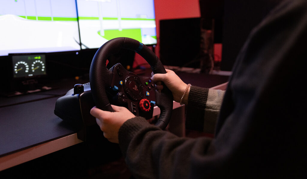 Two hands holding the steering wheel of a simulator designed to help older adults with driving.