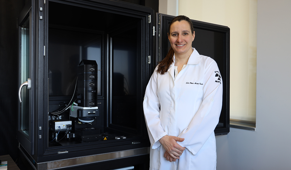 A woman wearing a labcoat poses for a photo while standing next to lab equipment.