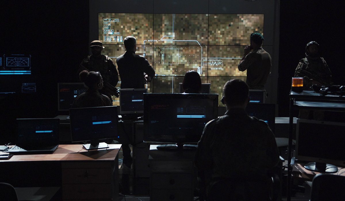 Group of soldiers or spies in dark room with large monitors and advanced satellite communication technology.