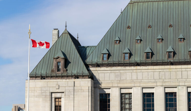 A side view of an older looking offic building with a Canadian flag flying off a large pole next to it.