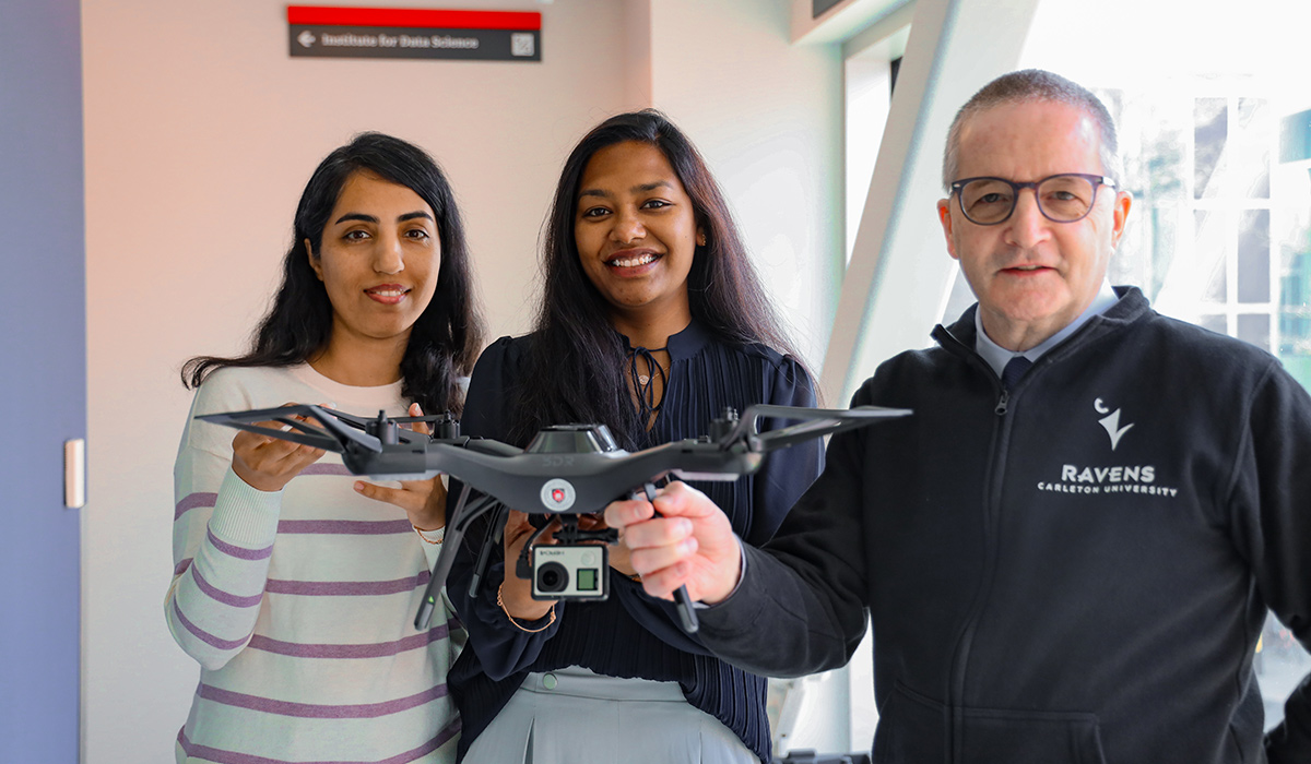 Three people pose for a photo while holding up a drone.