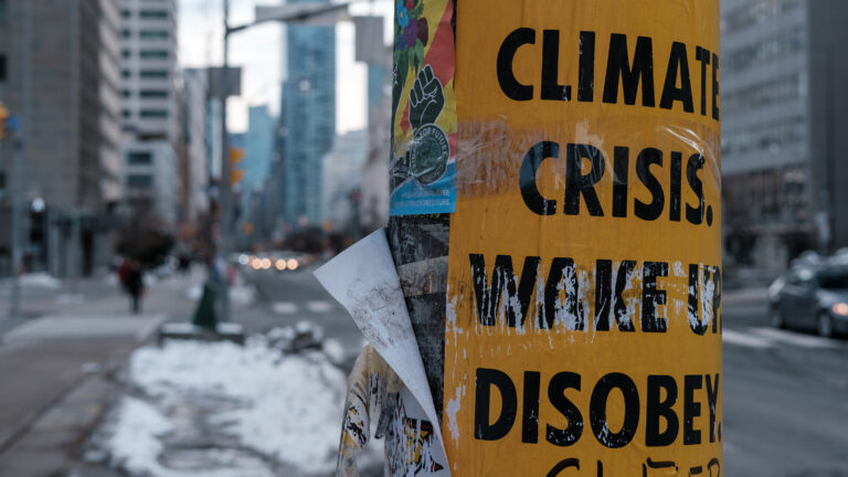 Close up of a climate change activism poster on a light pole with city landscape in the background