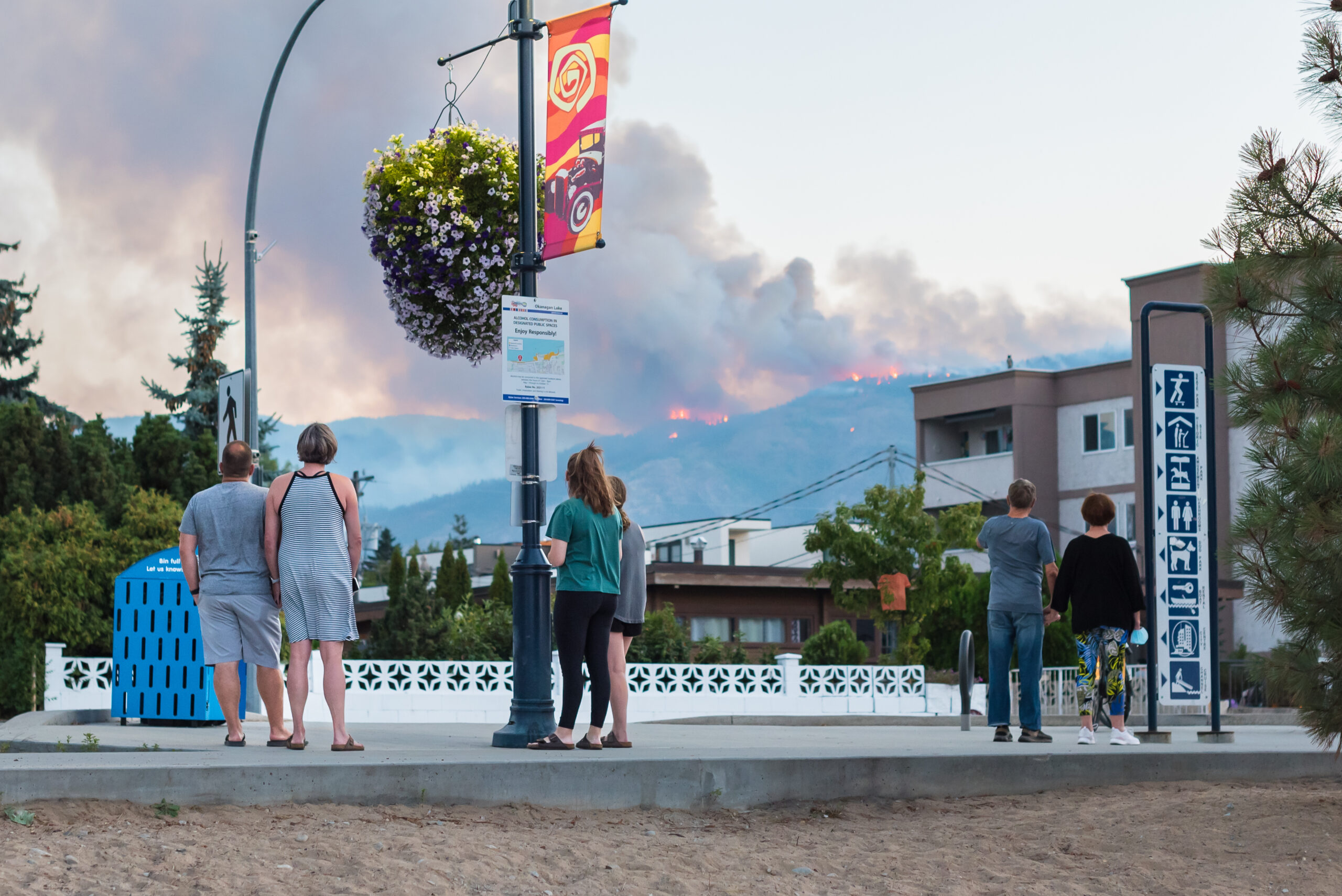 People watching forest fire in hills above city landscape.